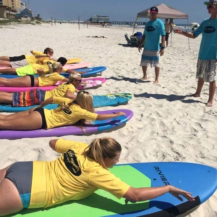 Students practicing prone paddling on boards on the beach