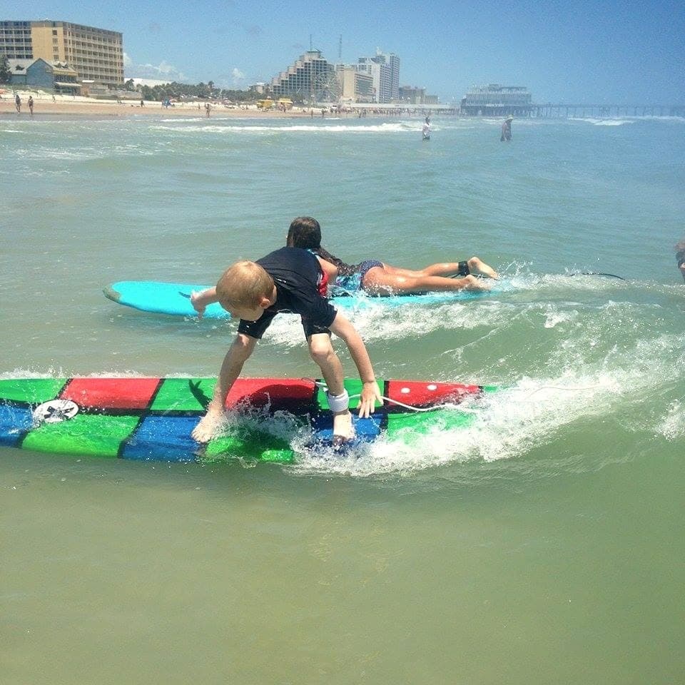 Young surfer riding whitewater toward the beach, seen from behind