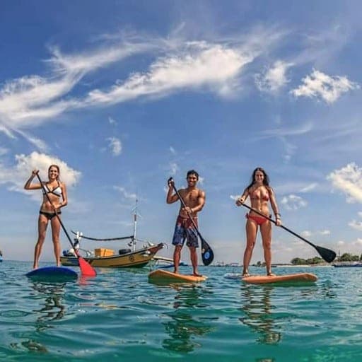 Three paddleboarders on flat turquoise water, fisheye view