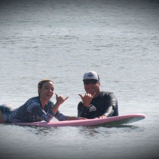 Student and instructor throwing shakas from surfboards in the lineup