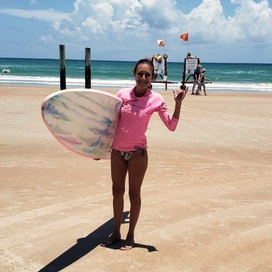 Student holding her board at the shoreline after a lesson
