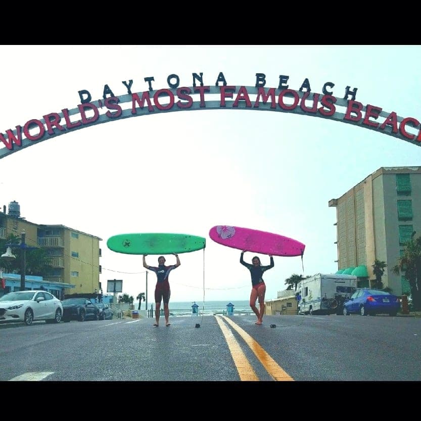 Surfers carrying boards under the Daytona Beach arch