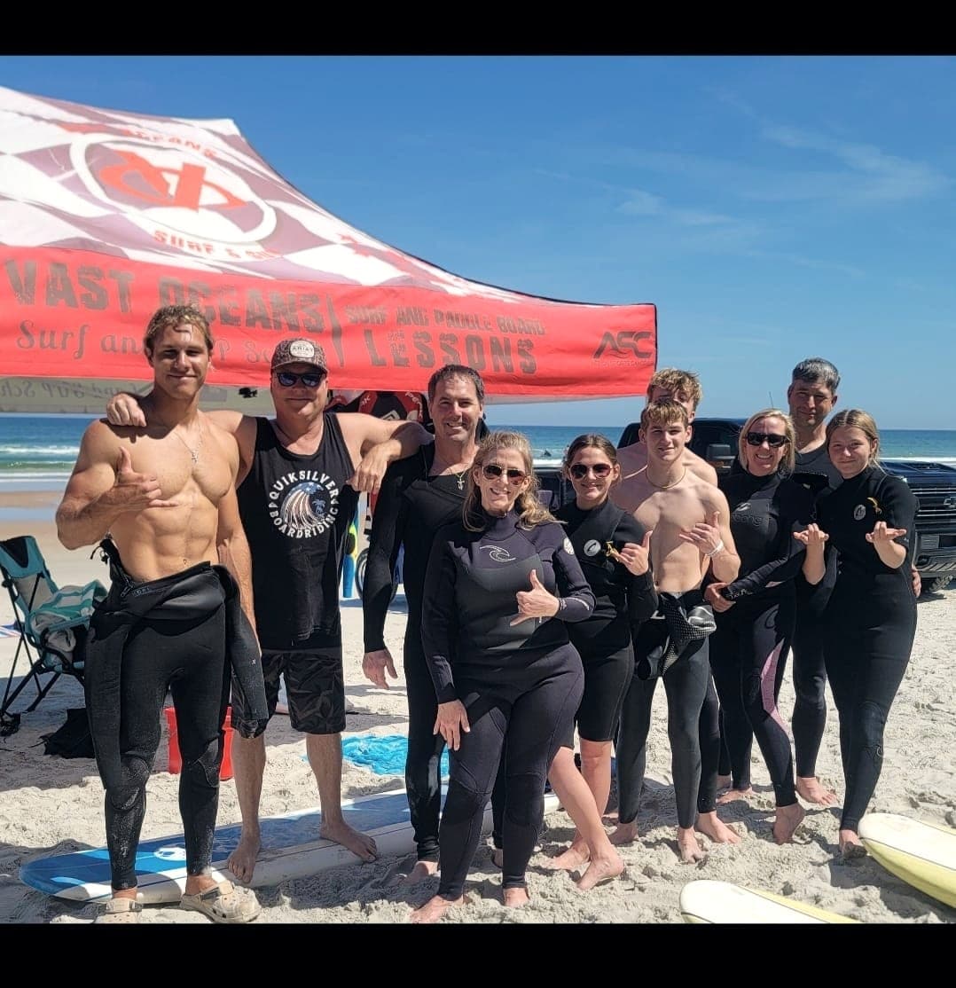 A group of adults after a lesson, most in wetsuits, standing under the Vast Oceans banner