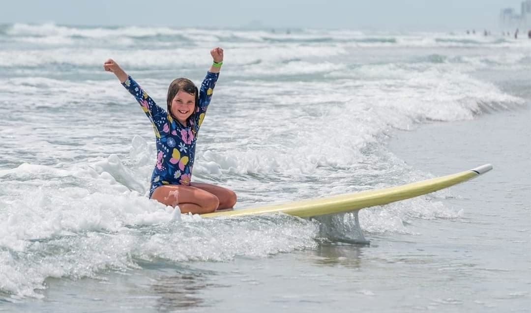 A young student riding a yellow board through the whitewater with one arm raised