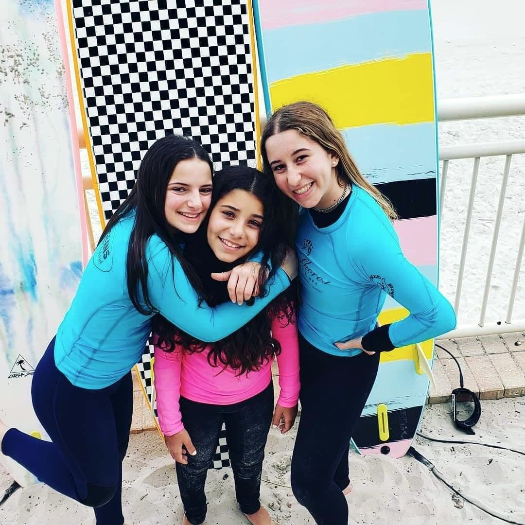 Three students in rash guards with their arms around each other, boards behind