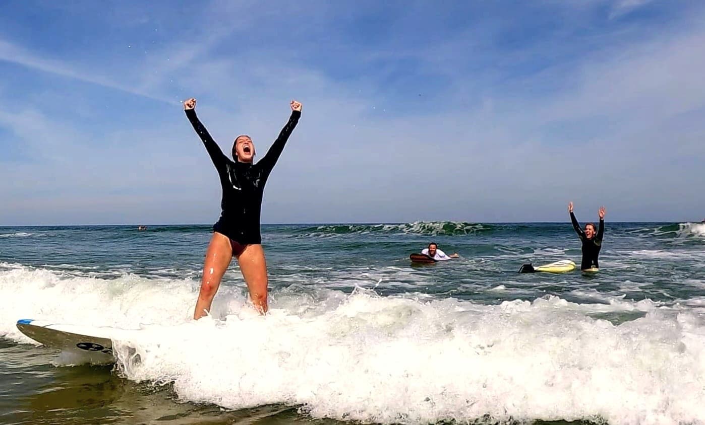 A student standing on a board in the whitewater with both arms raised