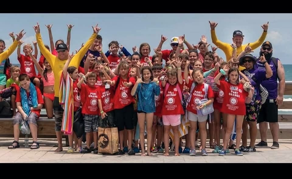 A large camp group in matching shirts with their arms raised