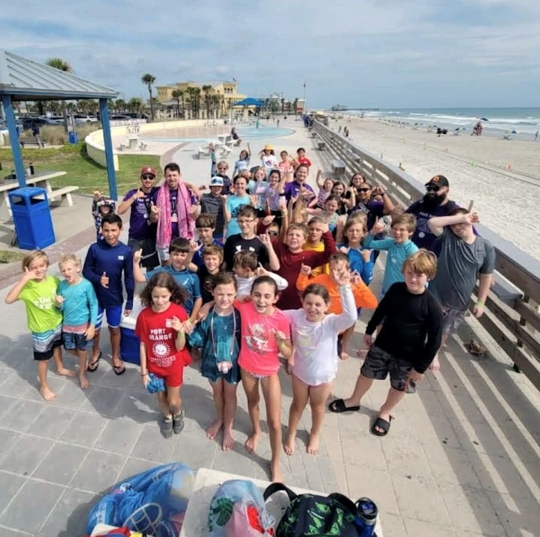 A large summer camp group gathered on the boardwalk with the beach behind