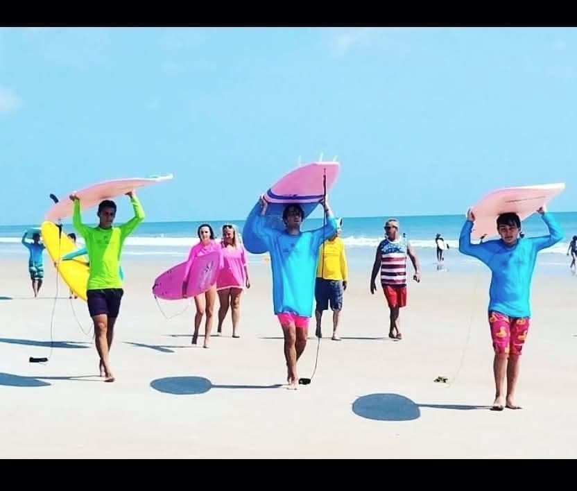 Students carrying soft-top boards on their heads along the beach