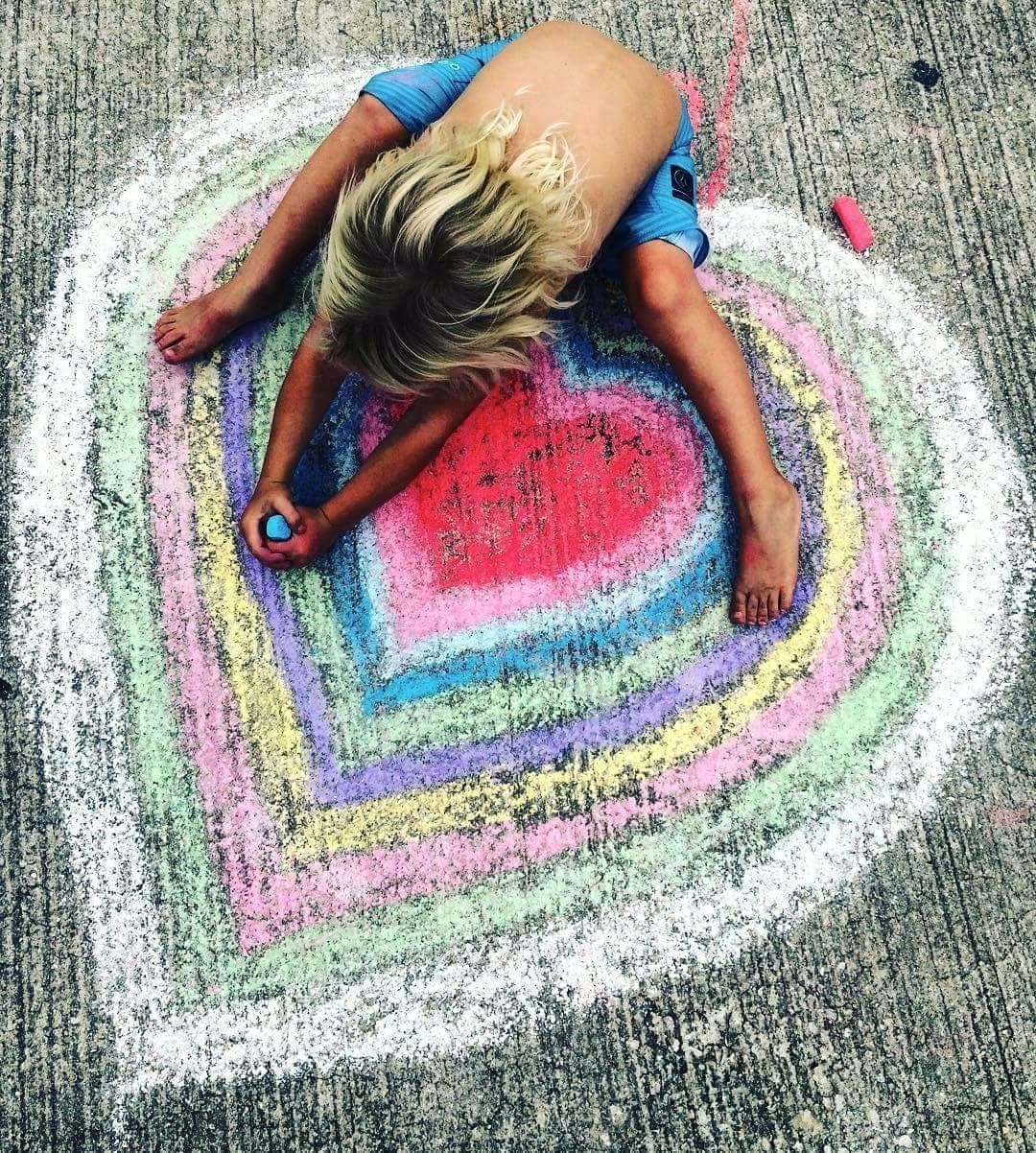 A child drawing a large chalk heart on the boardwalk, seen from above