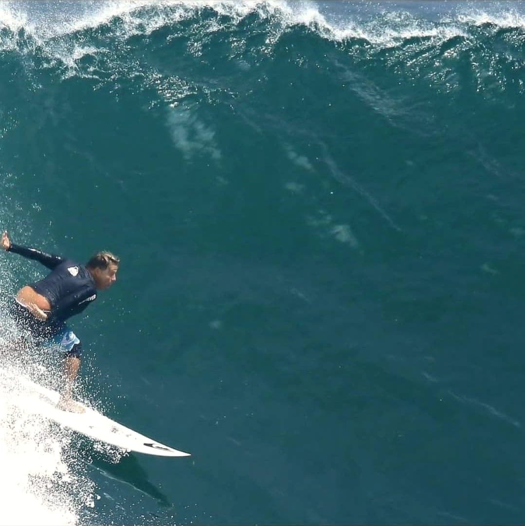 Ryan Ragan riding low across a steep green wave face