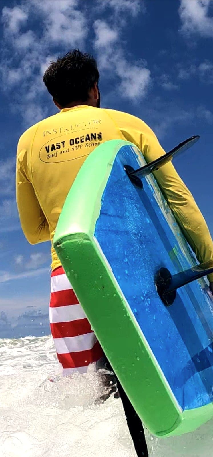 An instructor in a Vast Oceans shirt seen from behind carrying a soft-top board under one arm