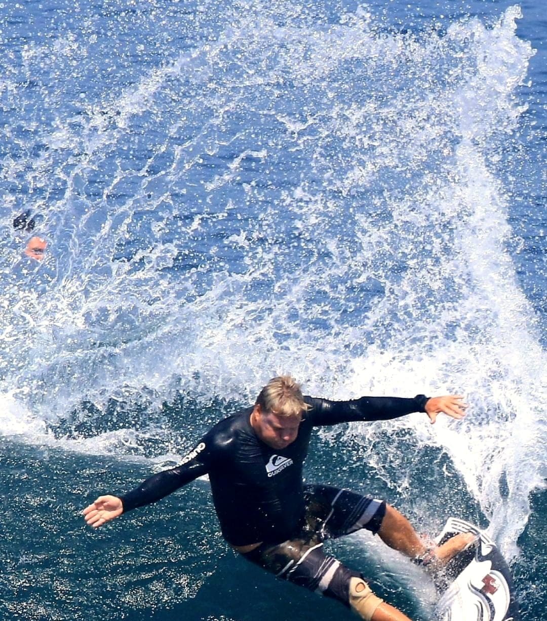 Ryan Ragan turning hard off the top of a wave in a wetsuit top, spray behind
