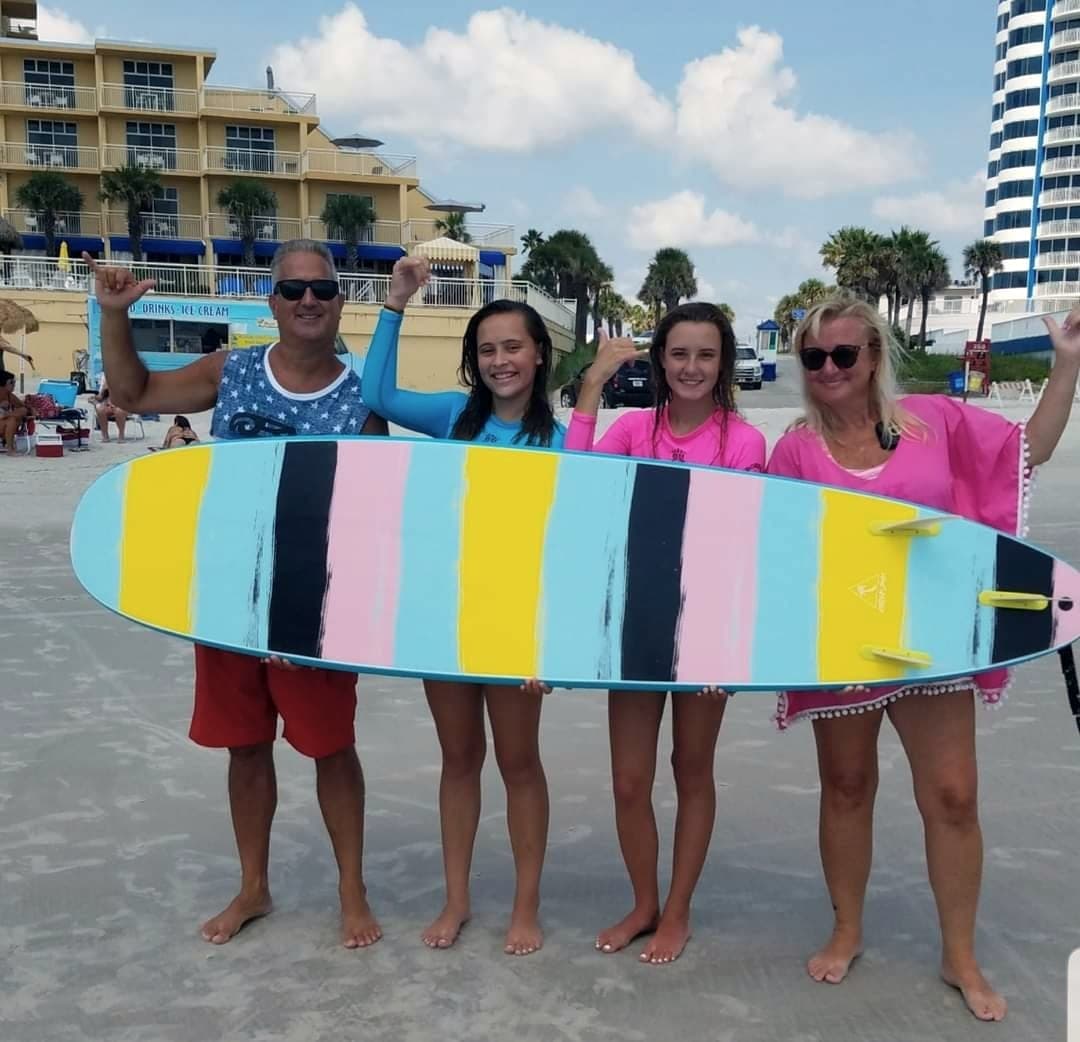 A group holding a striped longboard up together on the beach