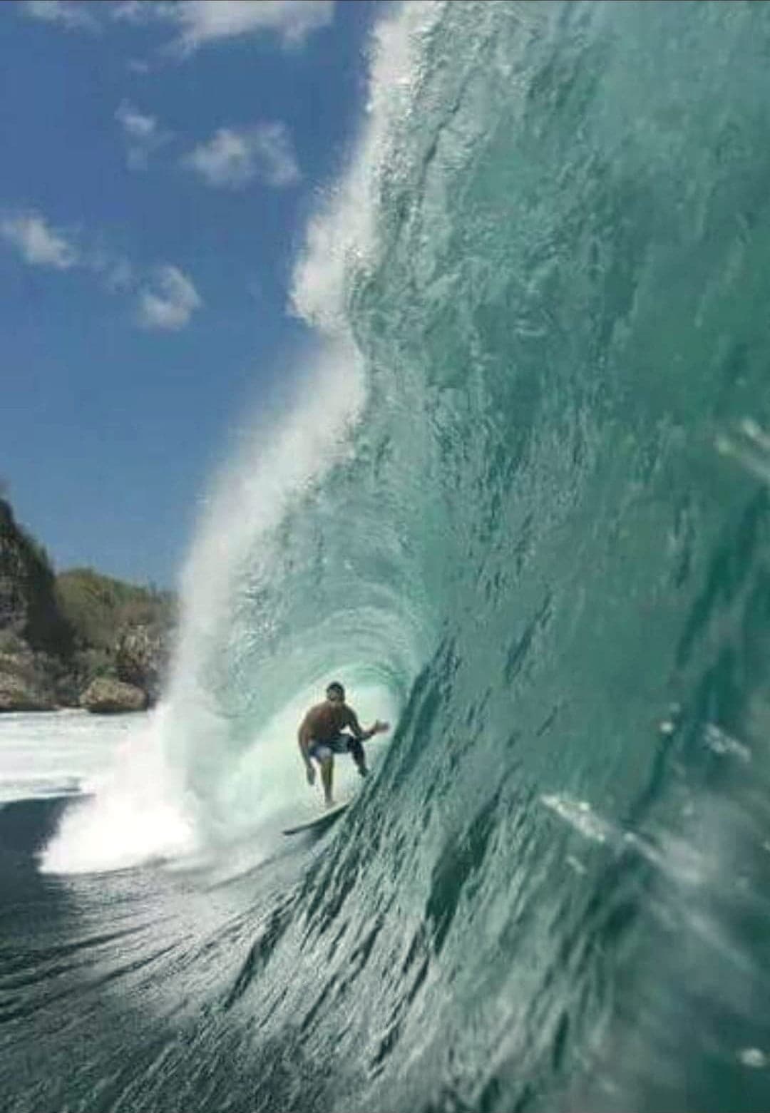 Ryan Ragan riding deep inside a large green barrel with cliffs behind