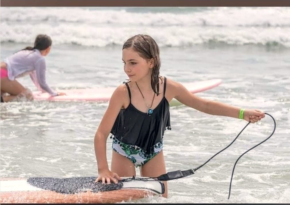 A student in shallow water with a hand on her board, holding the leash