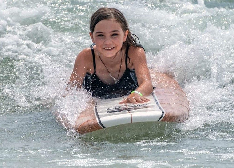 A young student riding a board prone through the whitewater