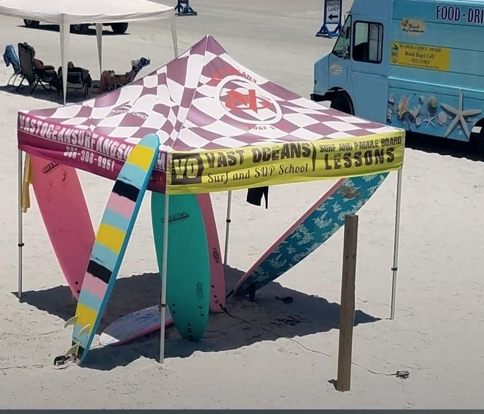 The Vast Oceans checkered tent on the sand with soft-top boards leaning against it