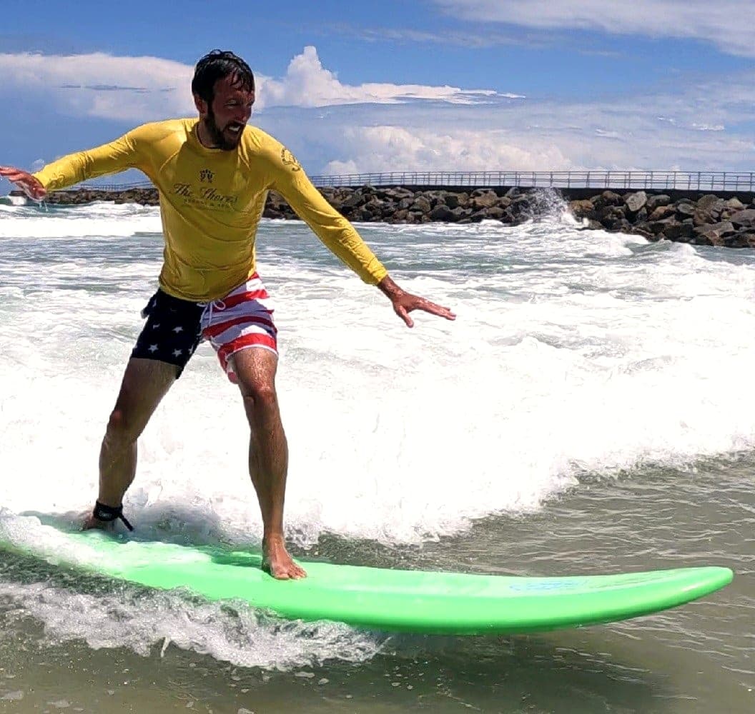 An adult surfer riding a soft-top board across a small wave