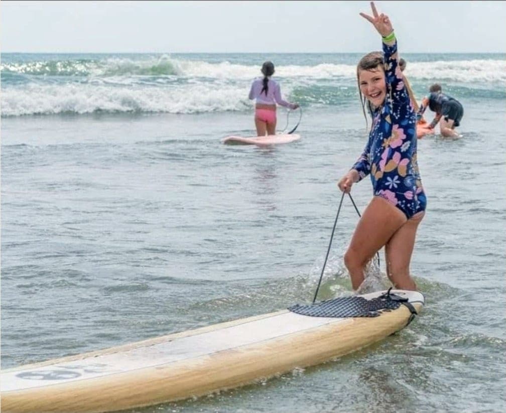 A student standing on a paddle board in shallow water with the paddle in hand, others behind