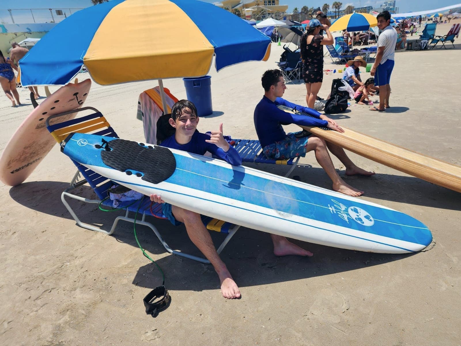 Two people sitting under a beach umbrella with surfboards propped beside them